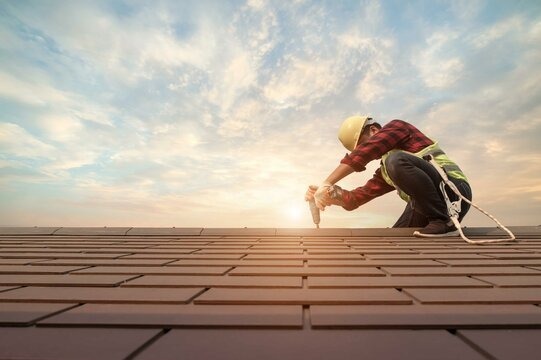 Roofer fastening shingles with precision drill at sunrise